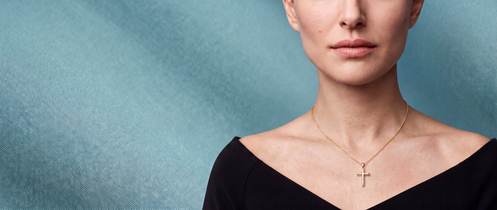 A SAINT GILD gold cross necklace worn on the collarbone