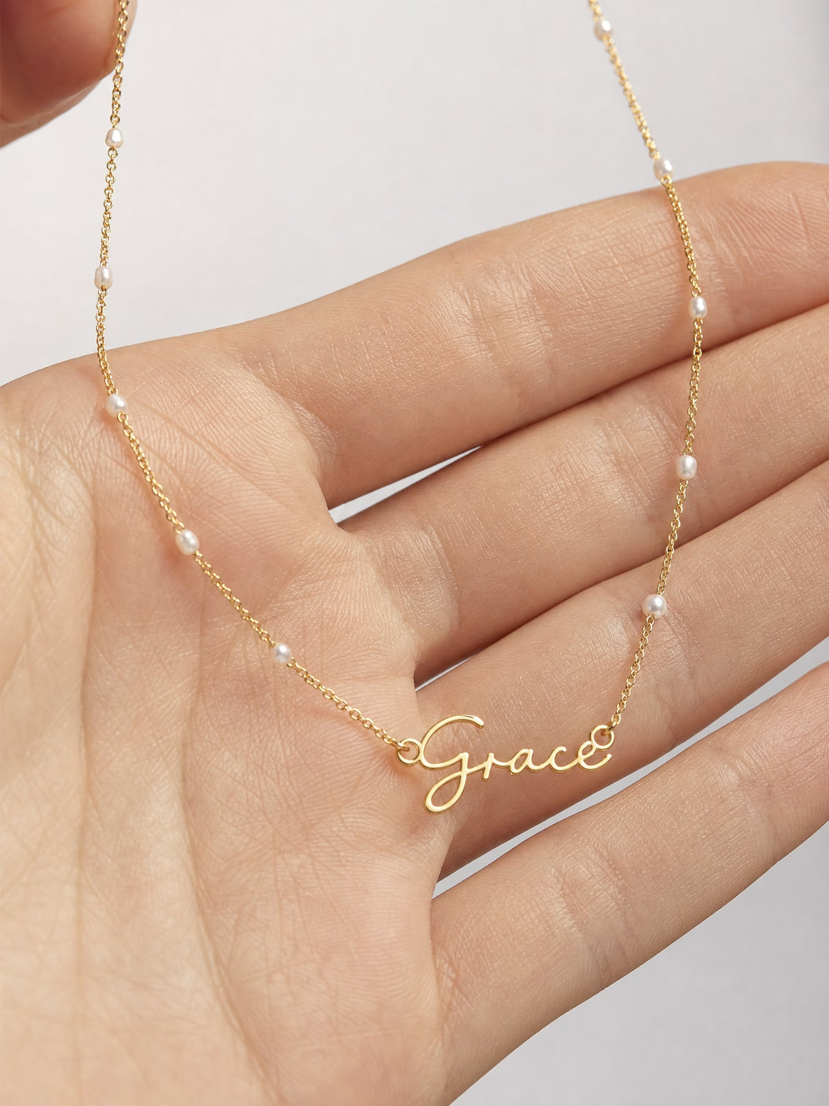 SAINT GILD faux pearl name necklace in hand