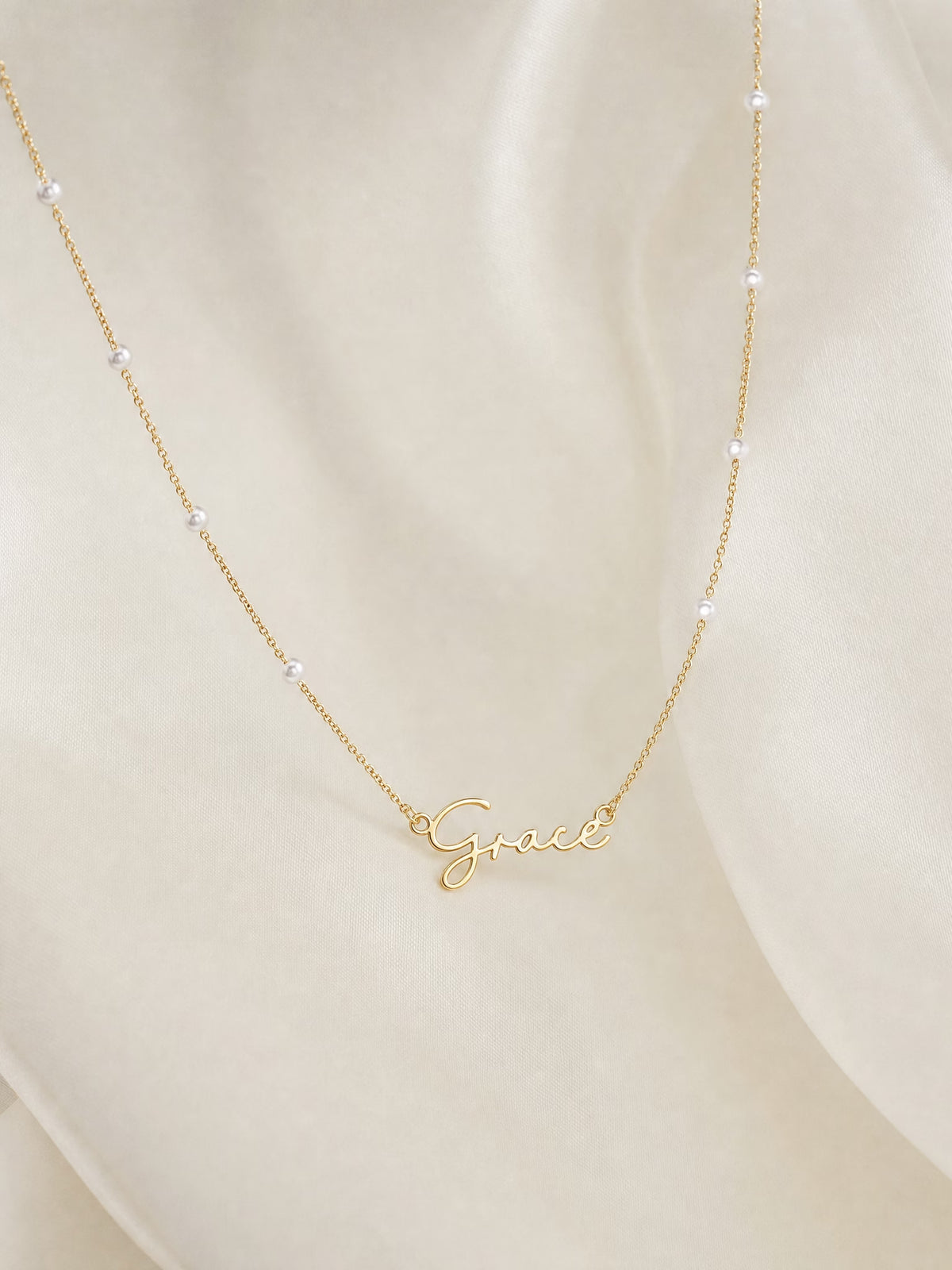 SAINT GILD faux pearl name necklace flatlay on satin