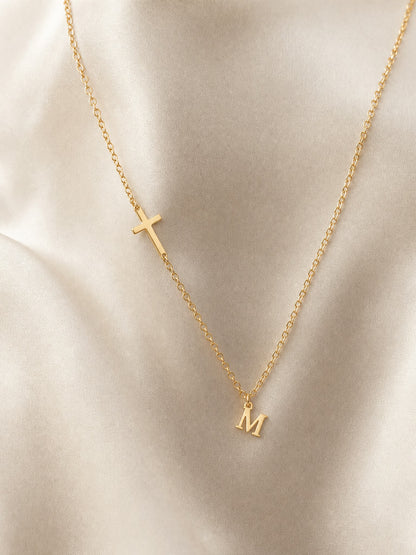 SAINT GILD initial cross necklace flatlay on satin