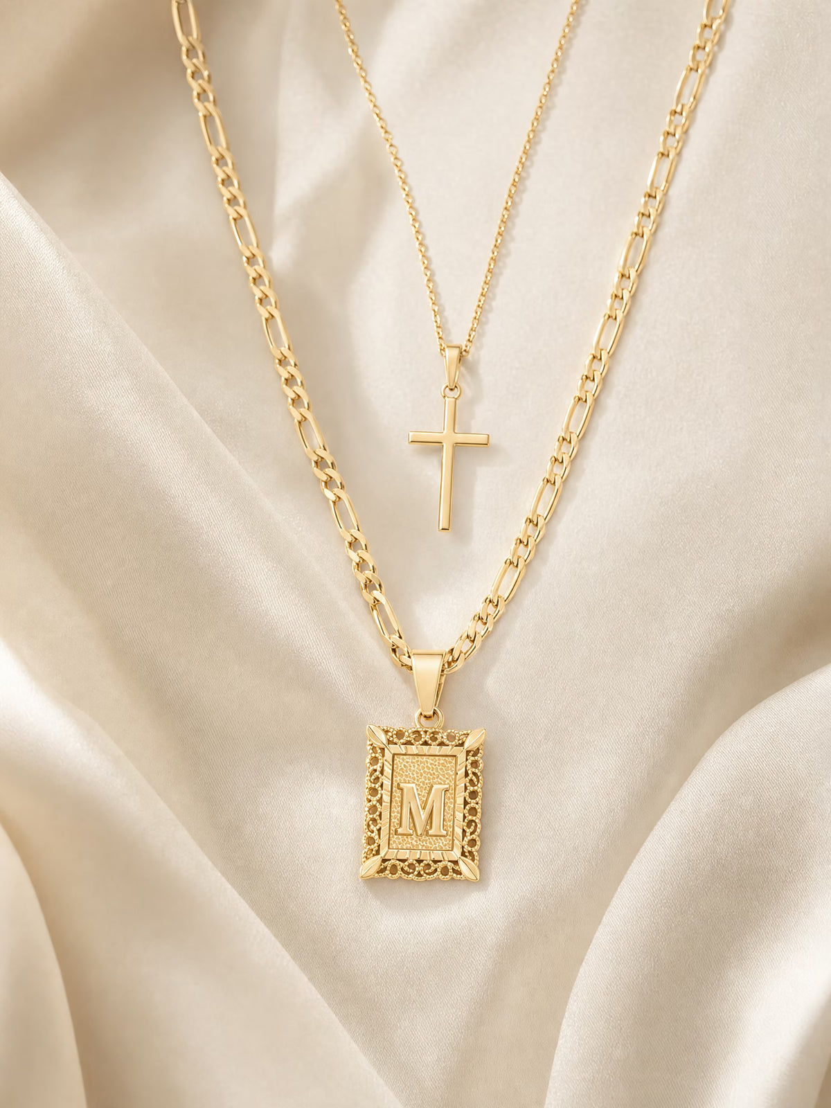 SAINT GILD initial cross necklace set flatlay on satin