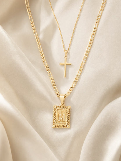 SAINT GILD initial cross necklace set flatlay on satin